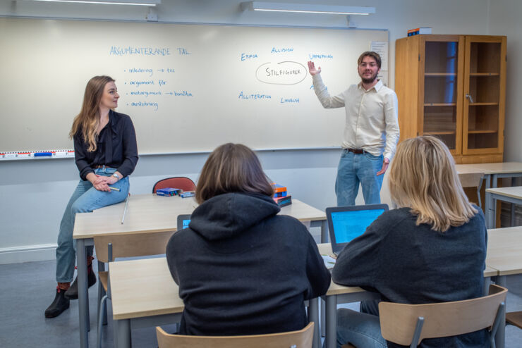 Två personer står och undervisar i ett klassrum. 