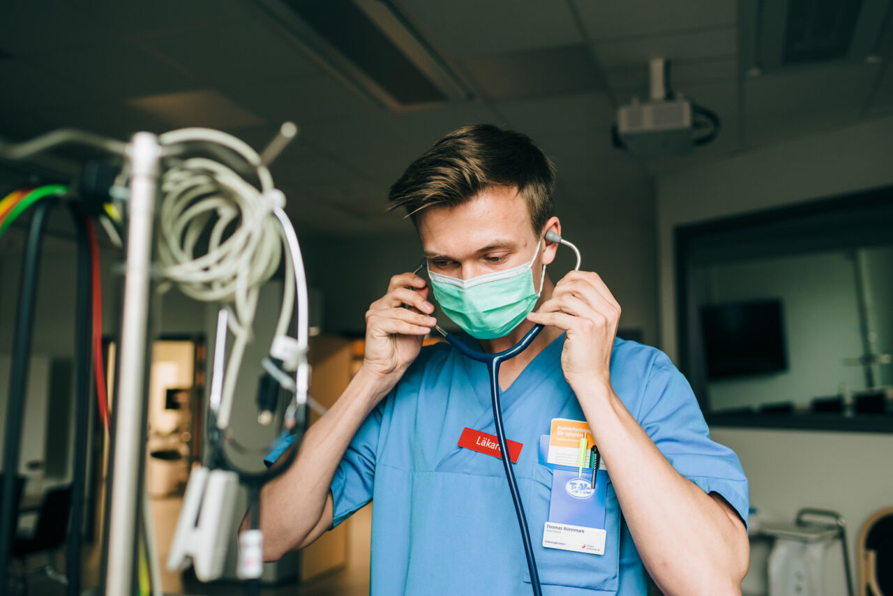 Ung man i läkarkläder sätter ett stetoskop mot öronen.
