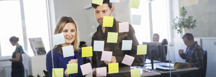 Två personer diskuterar framför en glasvägg med post-it-lappar.