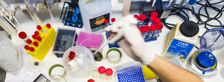 A hand with a white glove above test tubes and other equipment