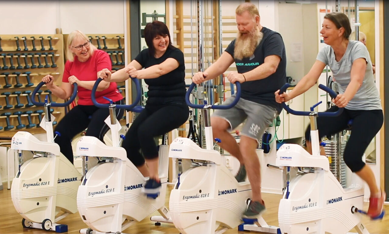 Three women and one man sitting on exercise bikes.