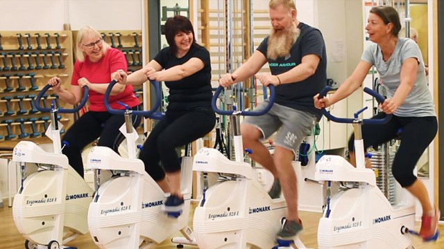 Three women and one man sitting on exercise bikes.