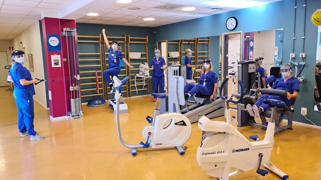 Fem sjuksköterskor som gör övningar i ett gym. Alla har operationsklädsel på sig.