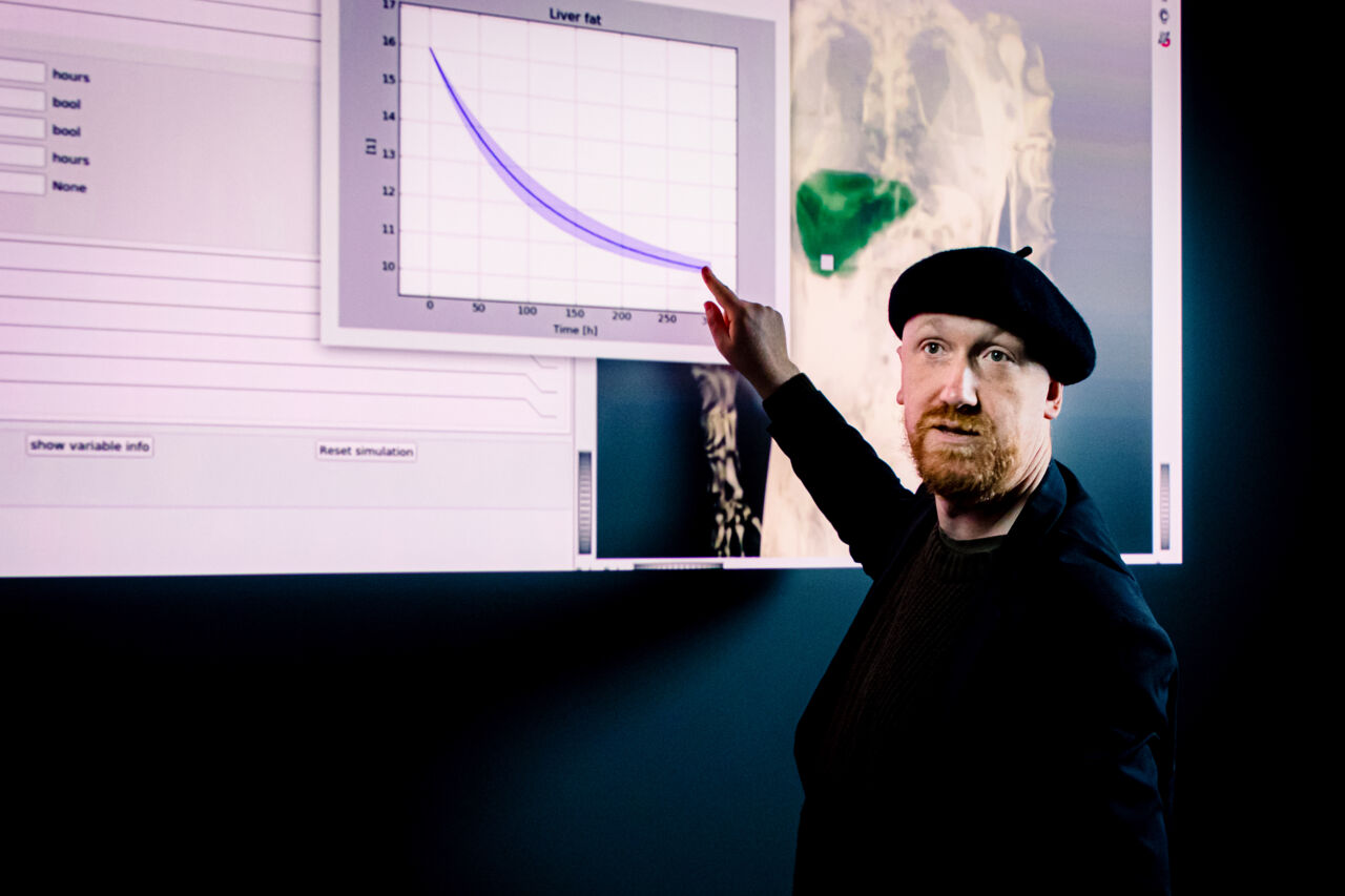 Gunnar Cedersund is standing in front of a screen and is pointing at a graph on the screen.