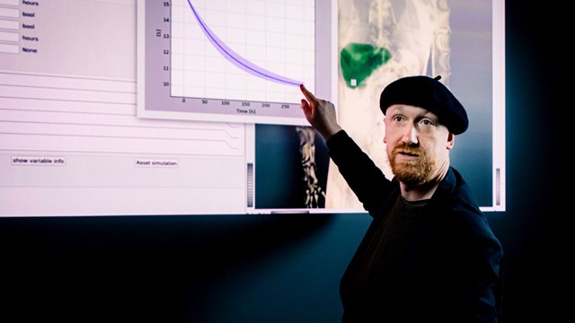 Gunnar Cedersund is standing in front of a screen and is pointing at a graph on the screen.