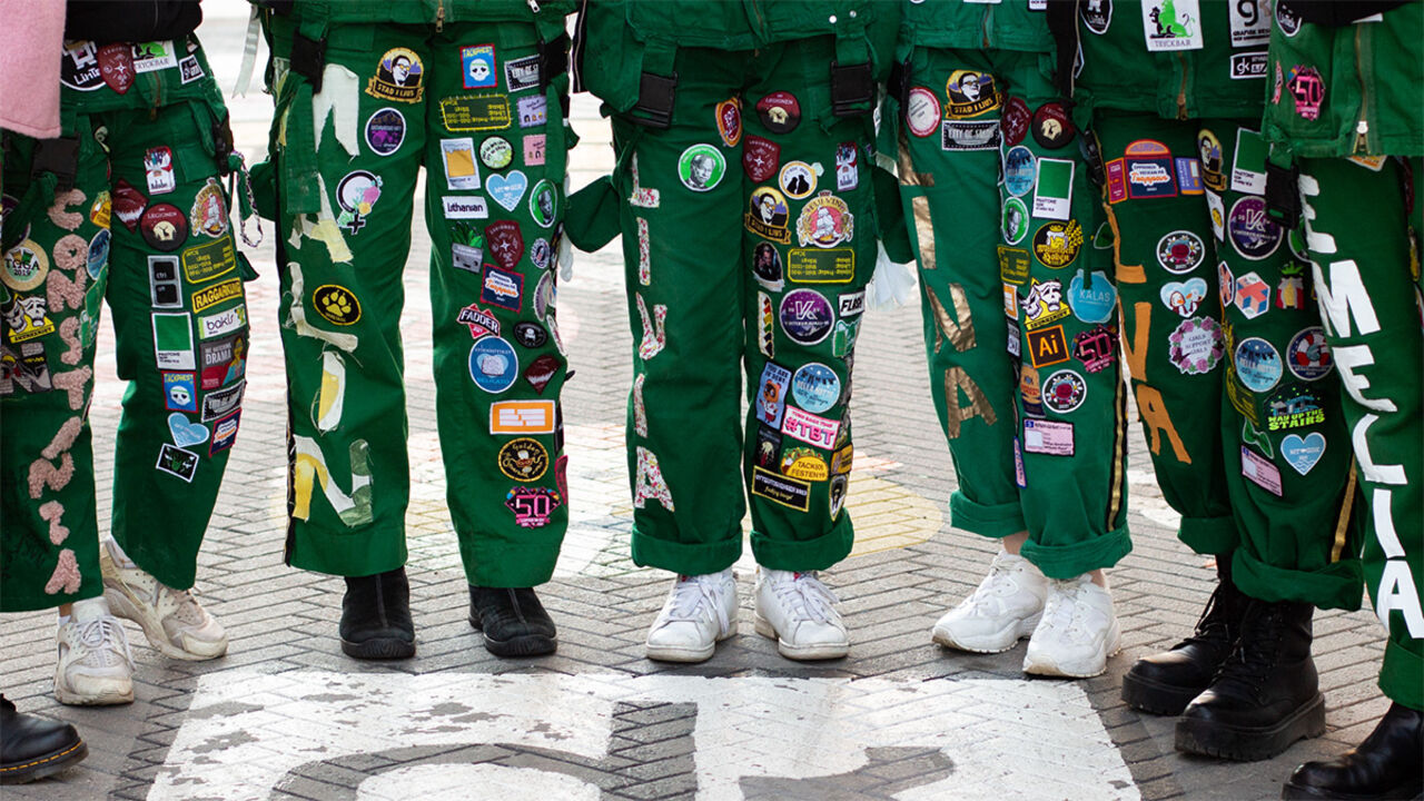 Studenter i gröna overaller med påsydda märken på benen