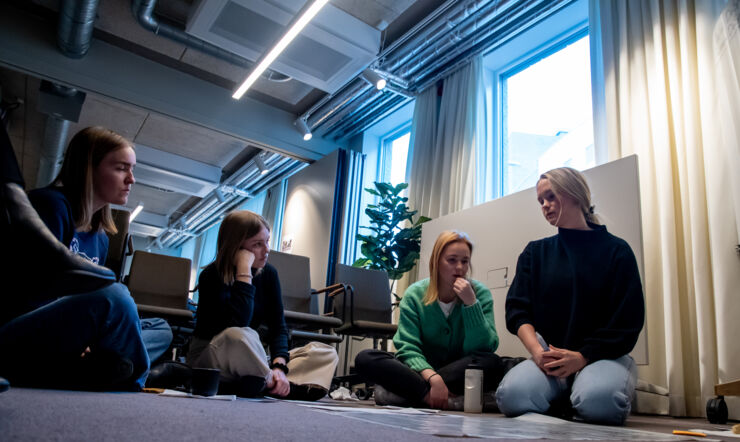 En grupp studenter jobbar aktivt med en case, de sitter på golvet