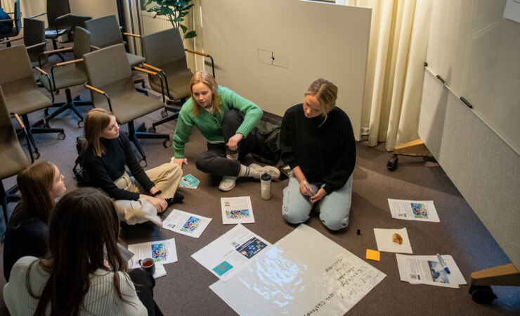 En grupp studenter jobbar aktivt med en case, de sitter på golvet