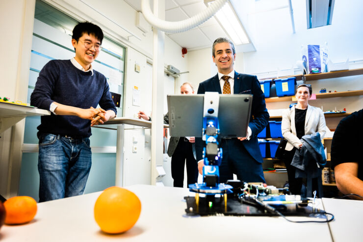 Chu Wanjun demonstrates for the group what fruits the robot can identify. In front of the robot lies an orange.