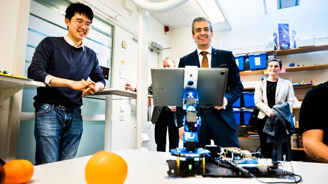 Chu Wanjun demonstrates for the group what fruits the robot can identify. In front of the robot lies an orange.