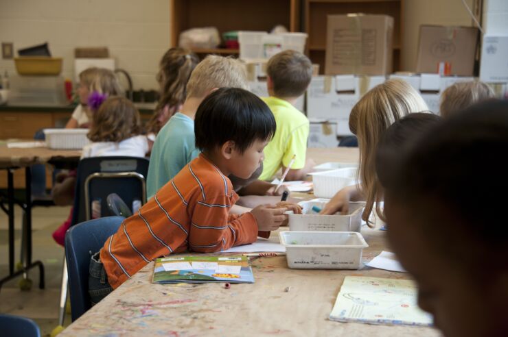 A classroom with children who sitts around table and  colours