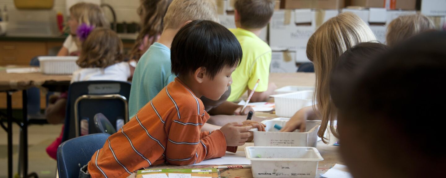 A classroom with children who sitts around table and  colours