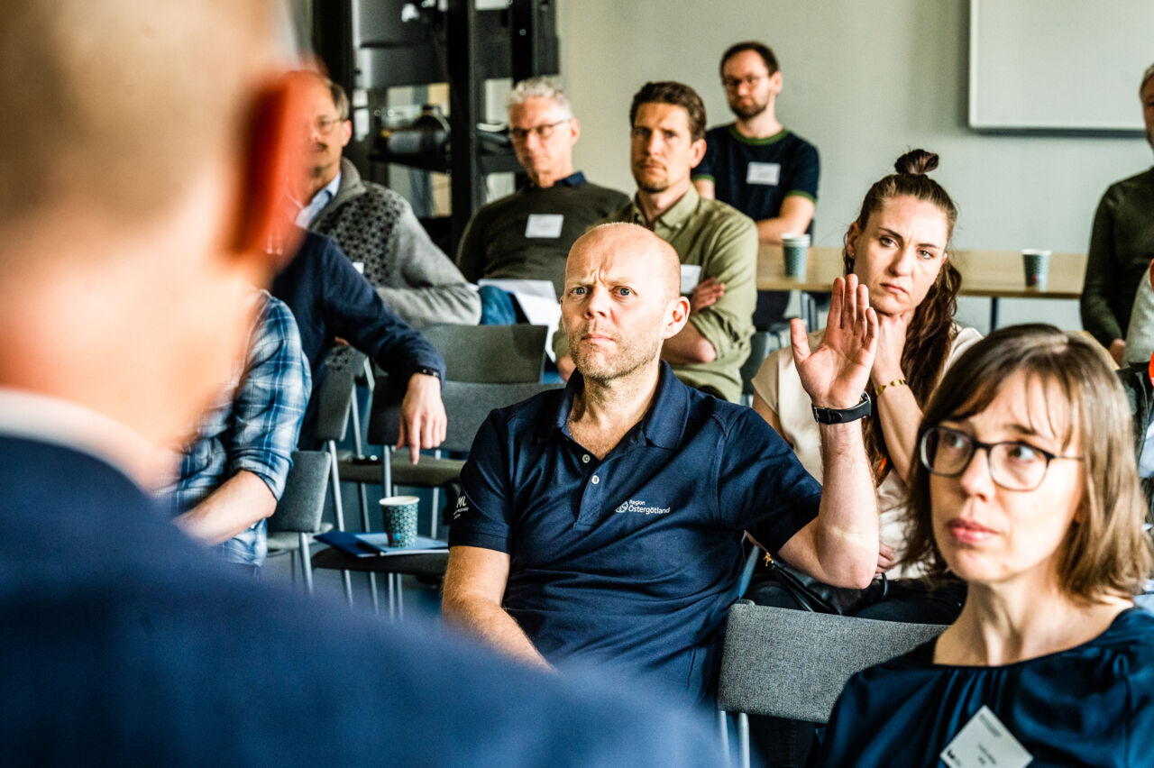 Människor lyssnar på en talare. En man räcker upp handen.