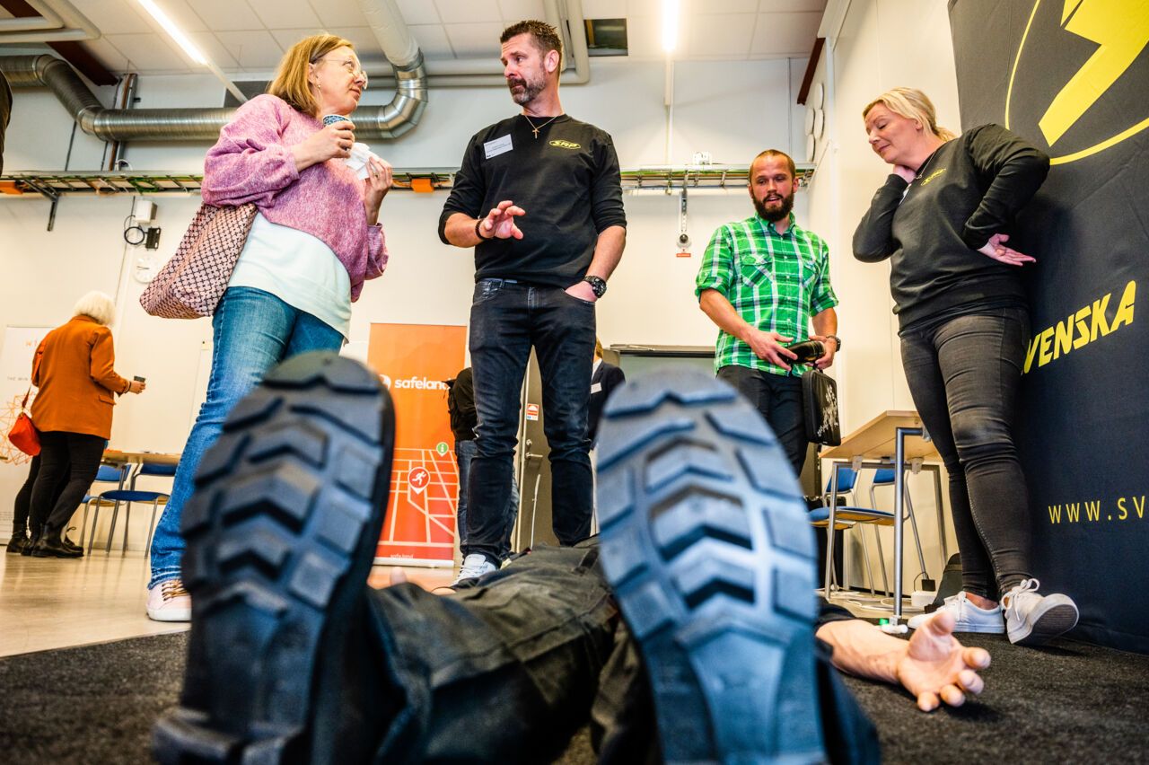 Människor i en mässhall, på golvet ligger en stor vuxen docka.