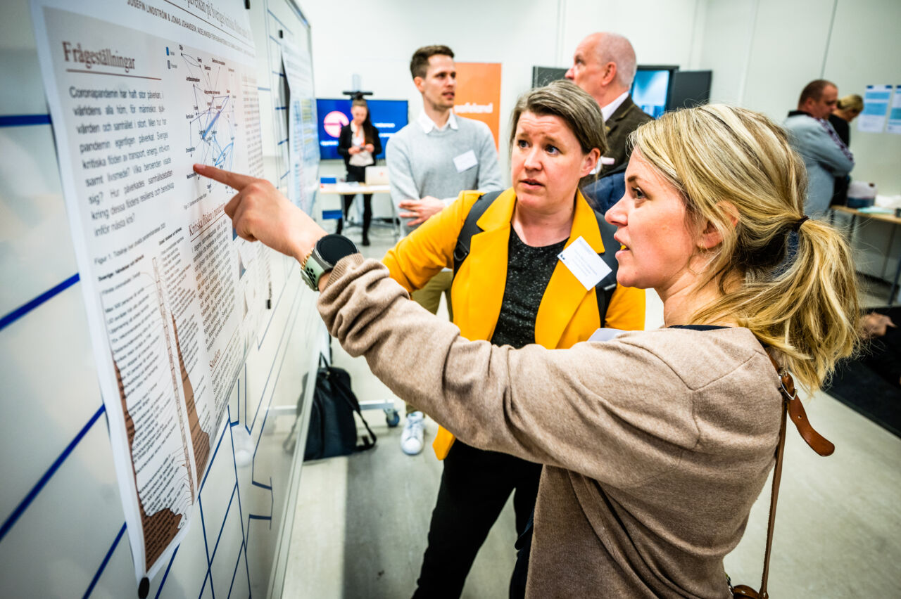 Två kvinnor tittar på konferensens program som sitter uppe på en vägg.