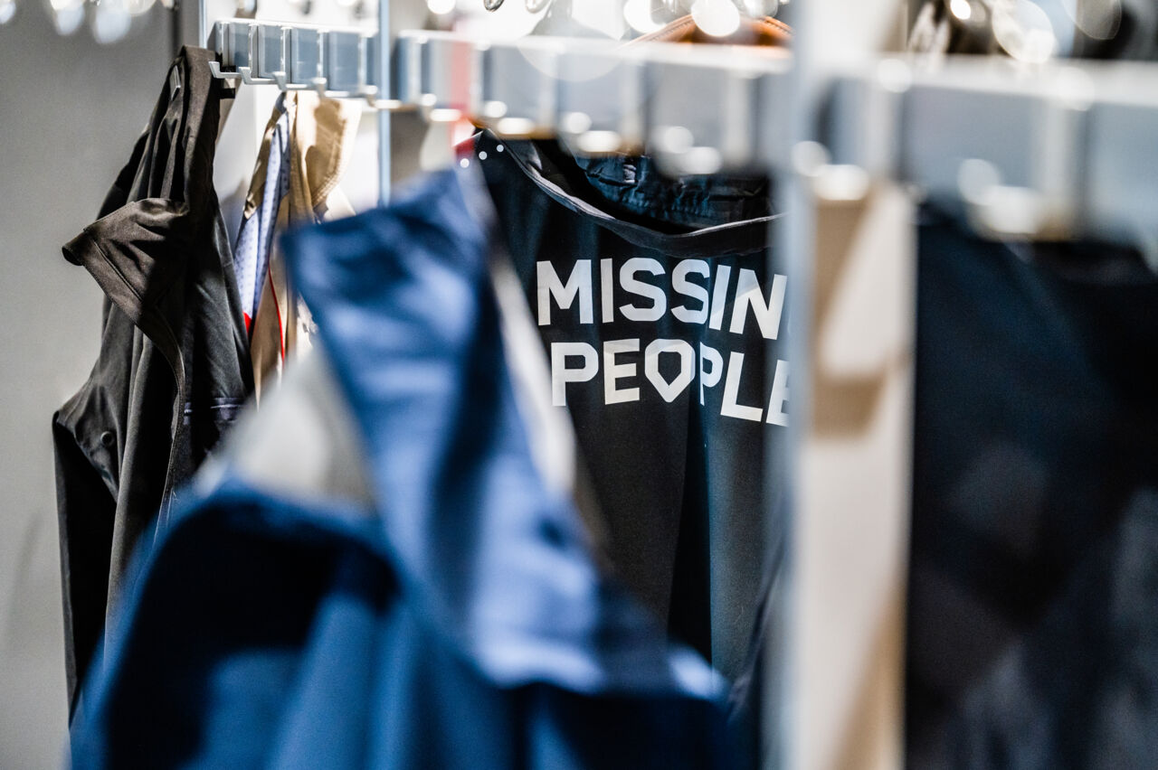 Klädhängare med flera jackor, en har texten Missing People. 