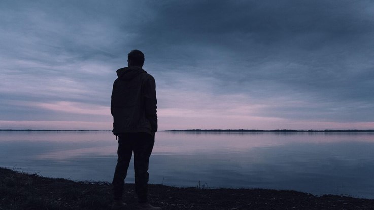 En person stående vid en sjö vid solnedgång.