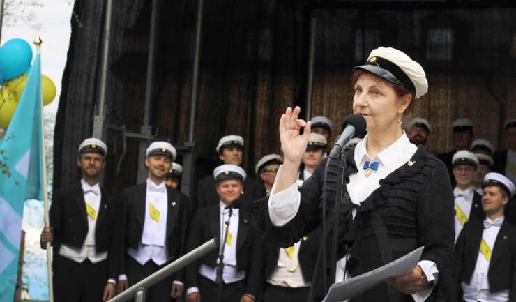 Woman in student hat orchestrating men´s choir.