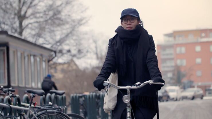 Young woman om bike; bicycles, cars and a building in the background