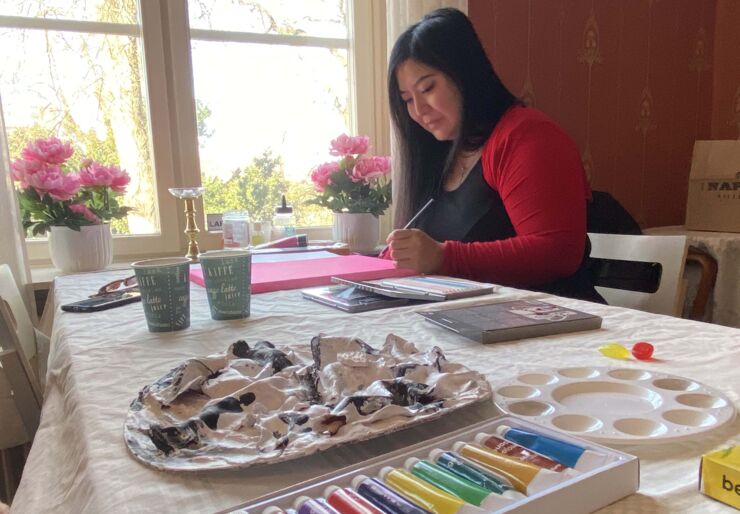 Foto på en person som målar. På bordet ligger färg och penslar.