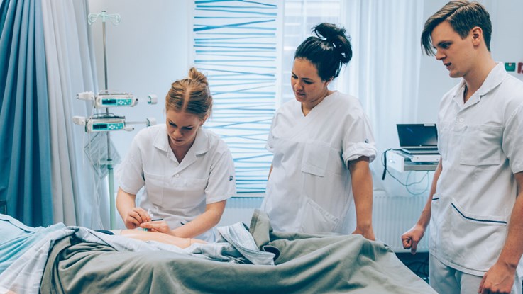 Tre sjuksköterskor syns i bild. En av dem sätter en nål på en patient medan de två andra ser på.