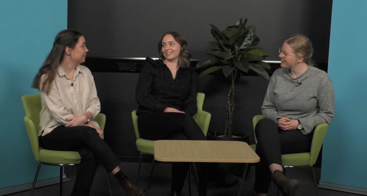 Tre kvinnliga studenter sitter och samtalar vid ett bord. Bakom dem står en rollup med budskap Linköpings universitet