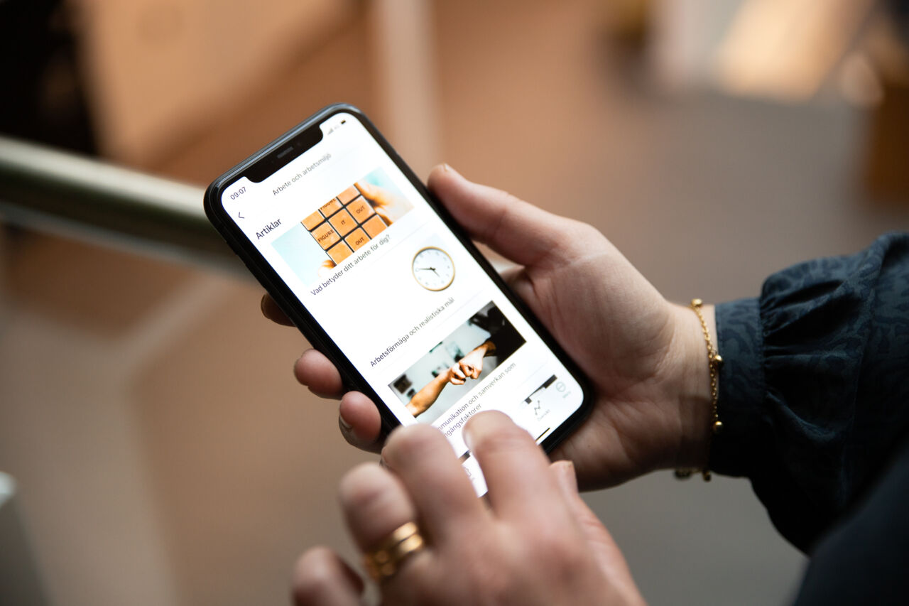 En hand håller i en telefon. På telefonen syns appen SWEPPE.