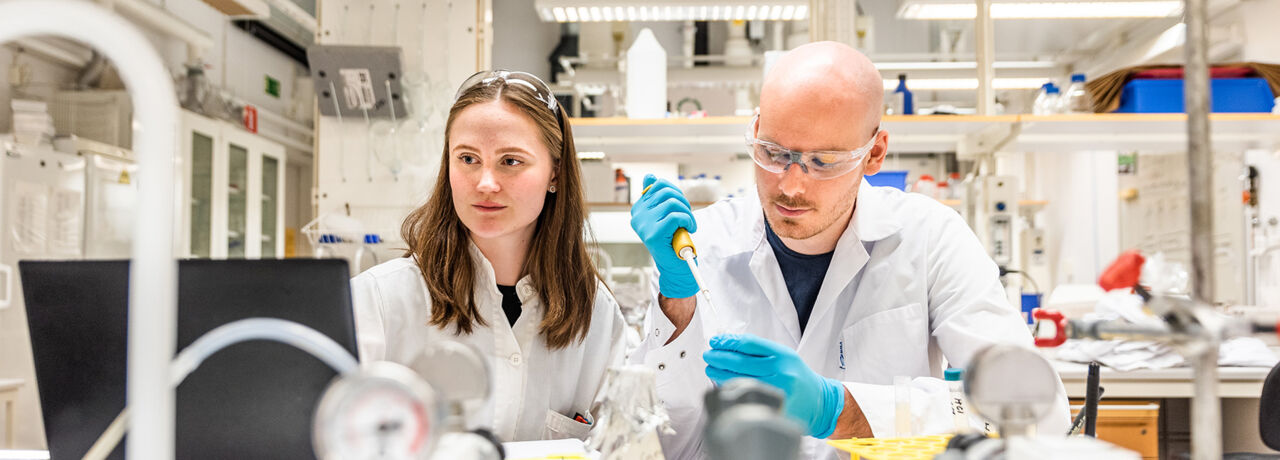 Två personer i vita skyddskläder i laboratorium