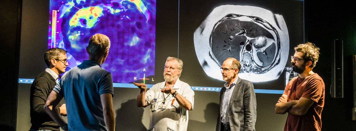 Five man are standing in front of a big screen showing MR images.