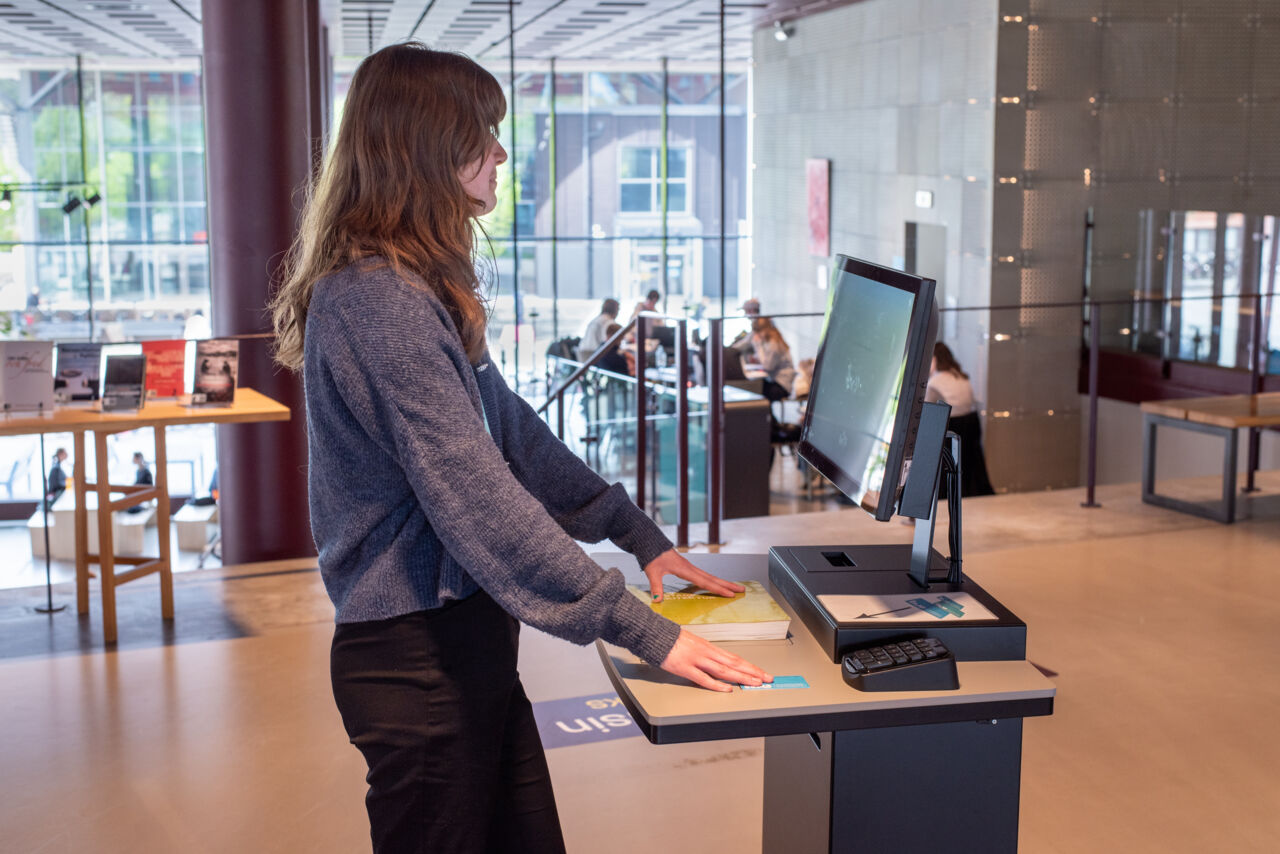 A female student borrowing a book at a self-check station.