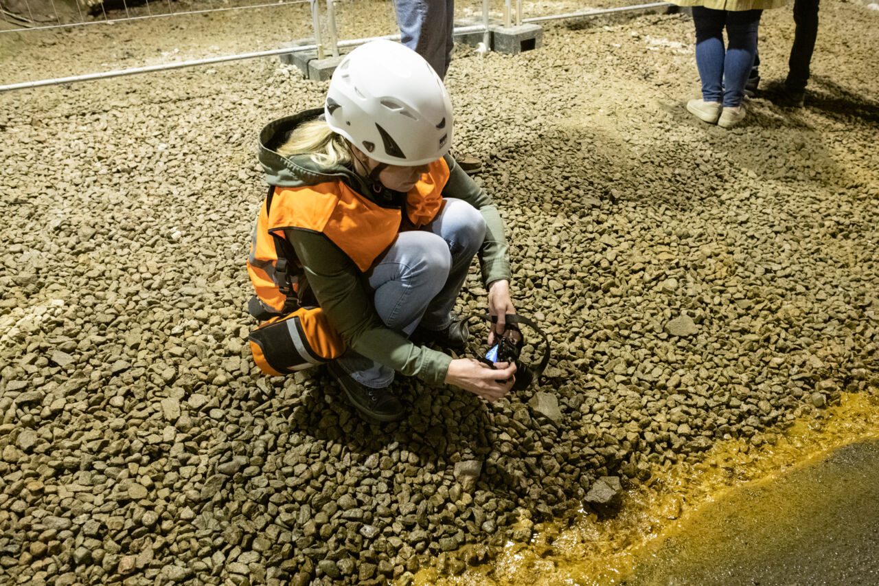 Kvinna i hjälm och orange väst sitter på huk.