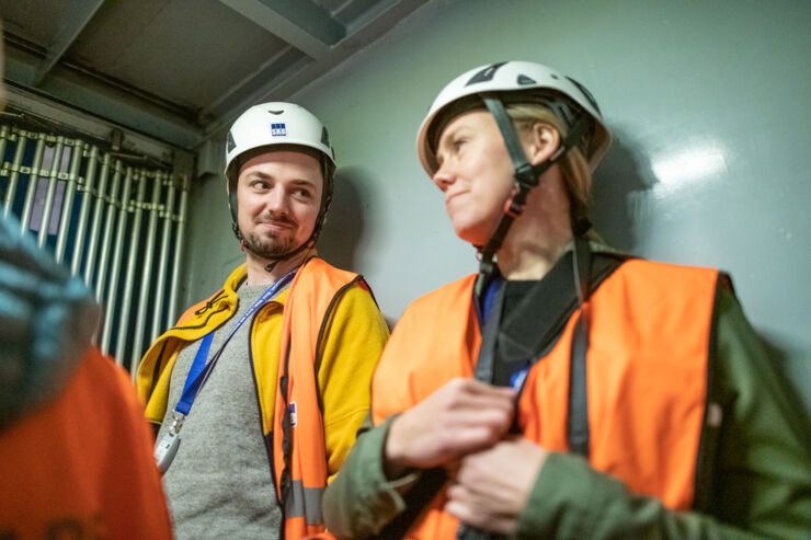 Man and woman wearing helmets and orange vests.