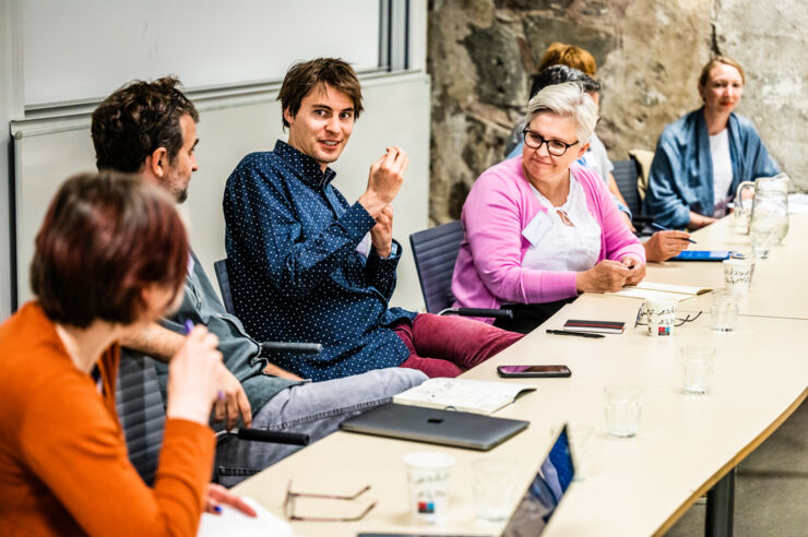 Four persons in the foreground discuss something, three persons are visible in the background. 