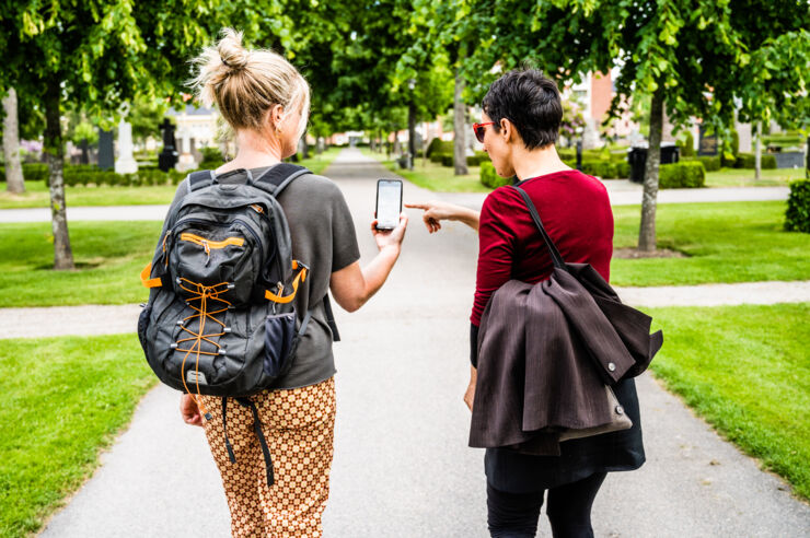 Two persons walk in a park and look at a smartphone. 