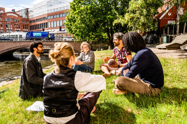 Five people are sitting on a lawn discussing.