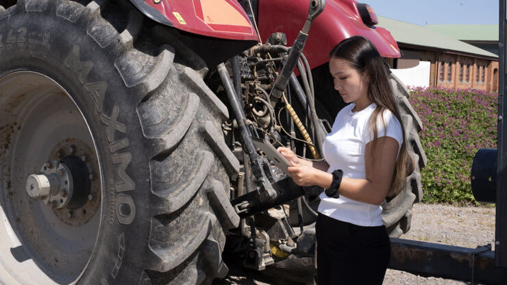 Ung kvinna står bredvid en traktor med en Ipad