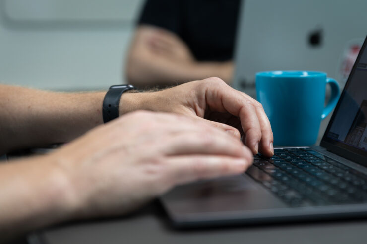 Två personer arbetar vid sina datorer, en blå kaffekopp syns emellan dem. 