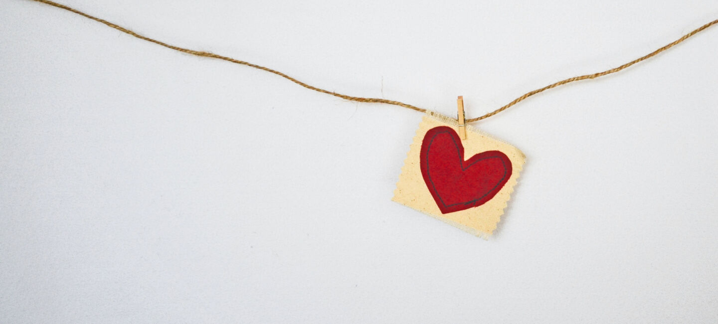 En lapp med ett hjärta hänger på en tråd mot en vit bakgrund.