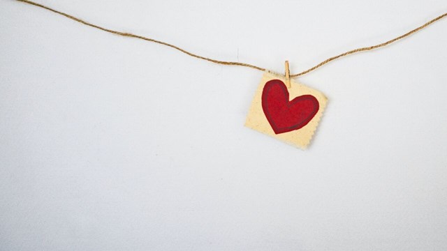 A heartshaped charm hanging on a gold thread.