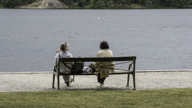 Two women sitting on a bench looking at the sea.