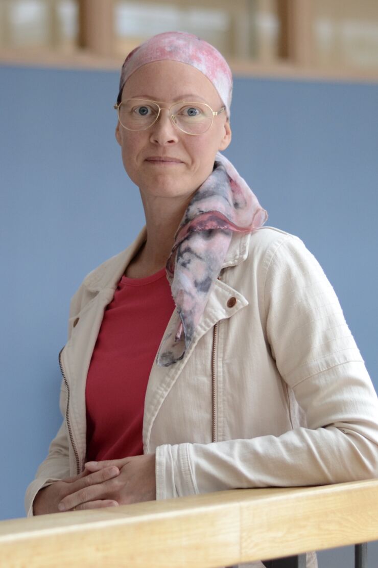 Inomhusporträtt av Pernilla Sundqvist som har en röd tröja, en vit jacka och bakgrunden är blå. 