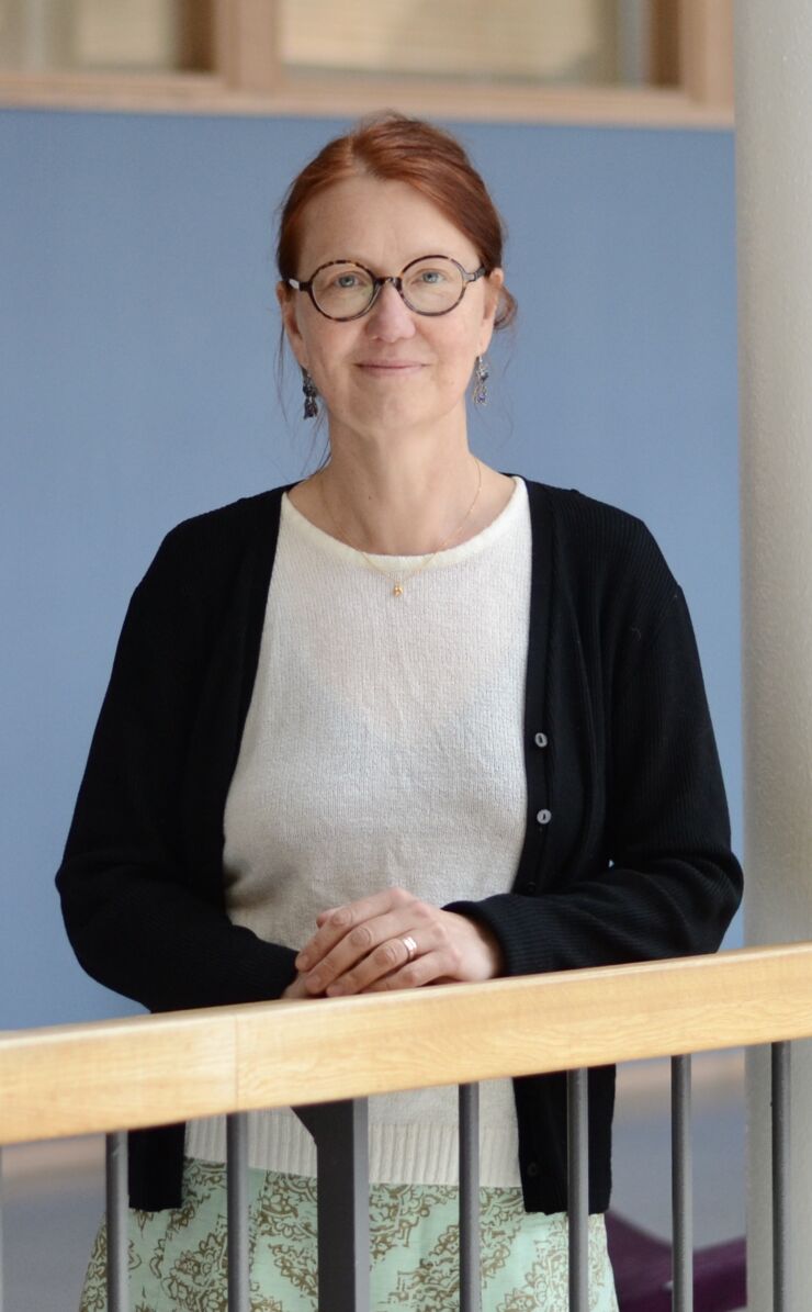 Porträtt av Susanne Engström som står inomhus klädd i vit topp och svart kofta. 