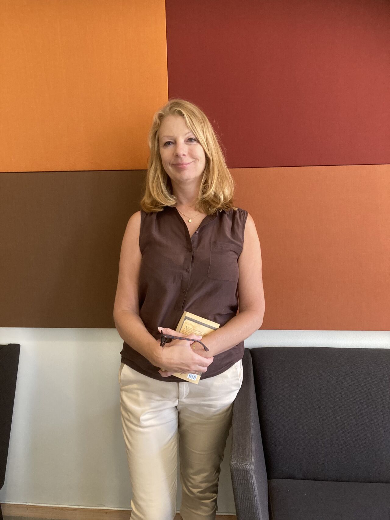 Katarina Rehder har en brun blus och beiga byxor mot en bakgrund av färgade textilrutor. 