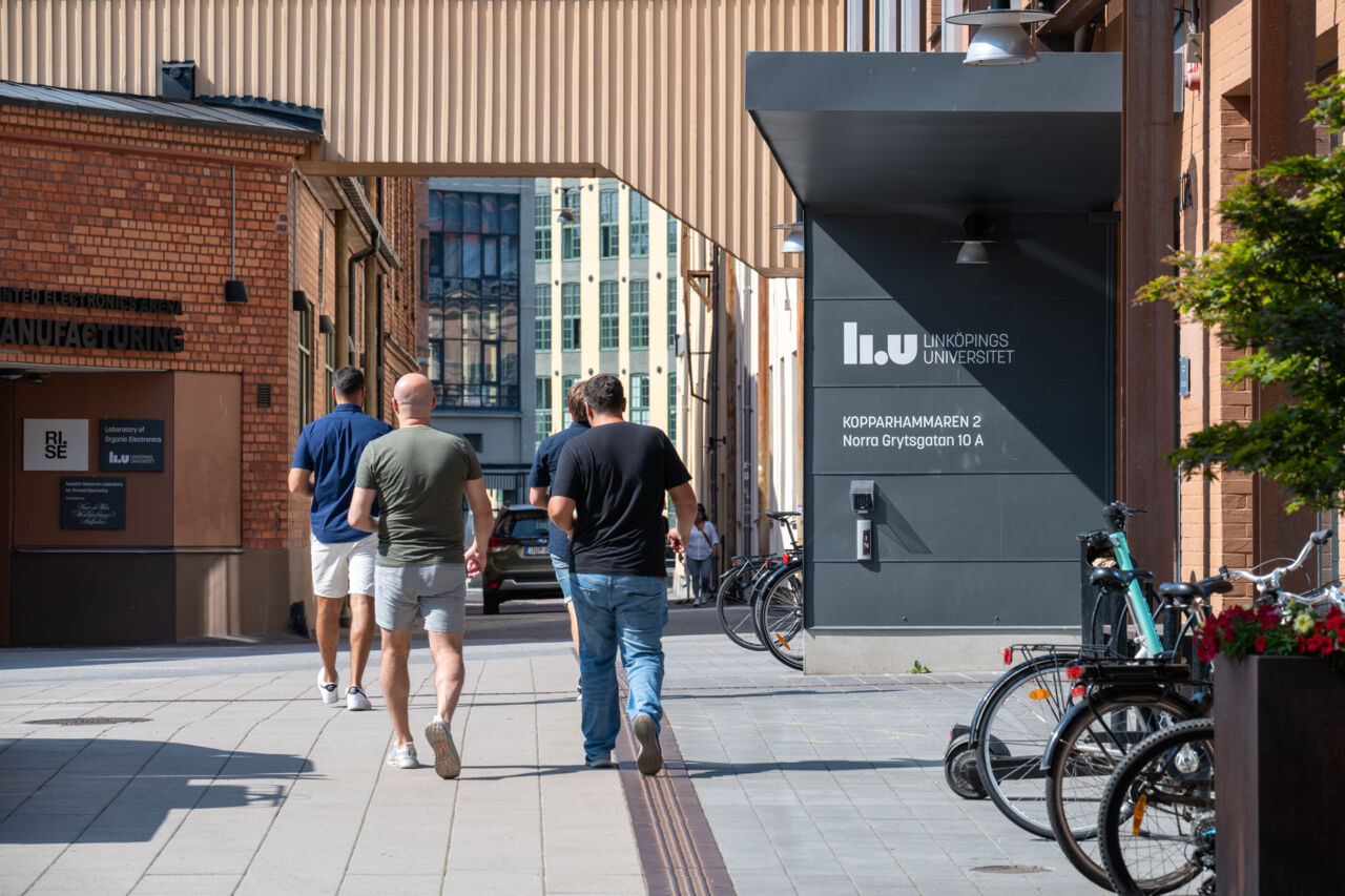 Män med ryggen mot kameran går mellan byggnader. Skylt: LiU Linköpings universitet Kopparhammaren 2