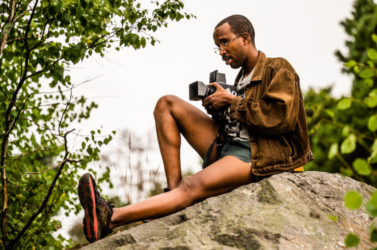 En person sitter med en kamera på en sten.