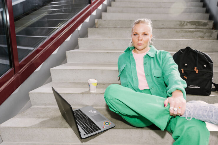 Student with laptop and backpack sitting on a staircase.