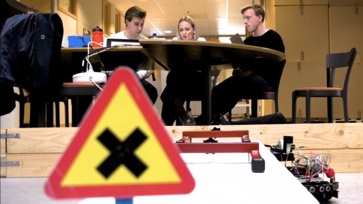 Vägmärke och robot i förgrunden. Studenter vid bord i bakgrunden