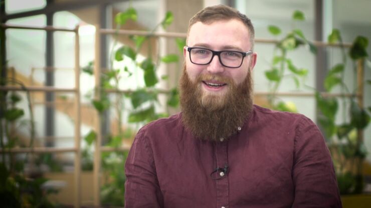 Skäggig och glasögonprydd manlig student med gröna växter i bakgrunden