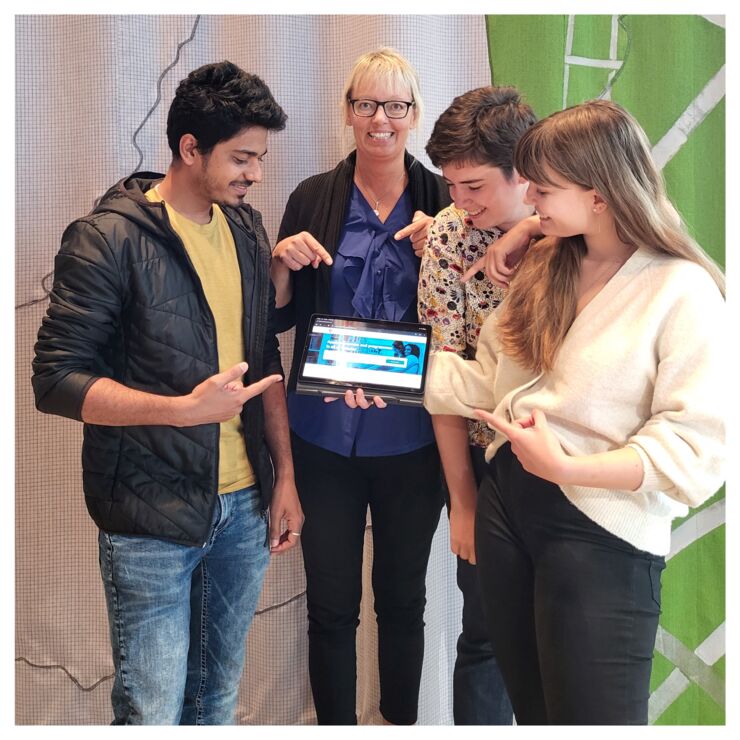 Four people standing together and pointing at tablet.