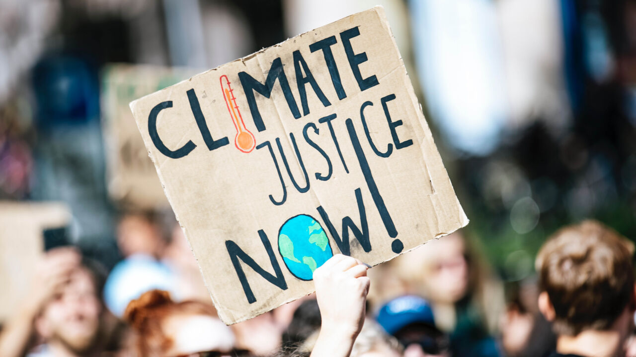 Demonstration. En en skylt med text på engelska Climate justice now i förgrunden.